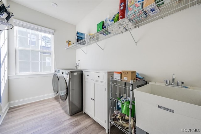 laundry area with baseboards, light wood-style flooring, cabinet space, a sink, and independent washer and dryer