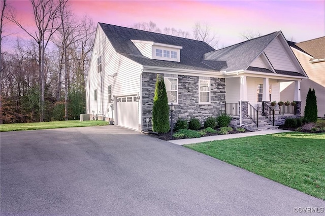 view of front of house featuring a lawn, aphalt driveway, stone siding, a porch, and a garage