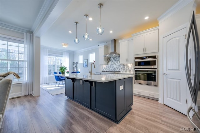 kitchen featuring crown molding, wall chimney range hood, light countertops, white cabinets, and stainless steel appliances