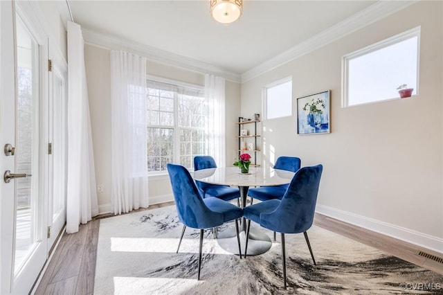 dining space featuring wood finished floors, a healthy amount of sunlight, visible vents, and ornamental molding