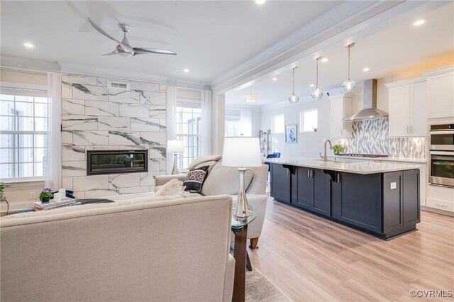 living room with crown molding, light wood-type flooring, recessed lighting, a fireplace, and a ceiling fan