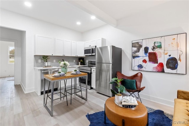 kitchen with beamed ceiling, backsplash, stainless steel appliances, light countertops, and baseboards