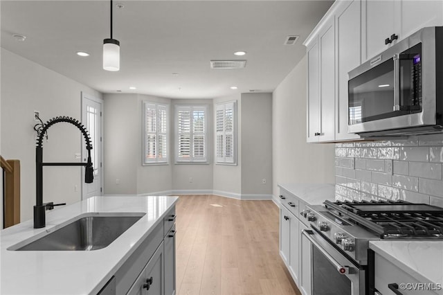 kitchen featuring tasteful backsplash, visible vents, light wood-type flooring, appliances with stainless steel finishes, and a sink