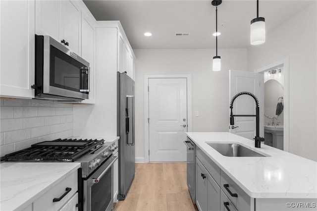 kitchen featuring visible vents, a center island with sink, a sink, tasteful backsplash, and stainless steel appliances