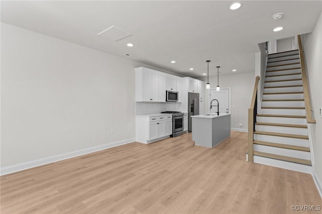 kitchen featuring light wood finished floors, tasteful backsplash, light countertops, white cabinets, and stainless steel appliances