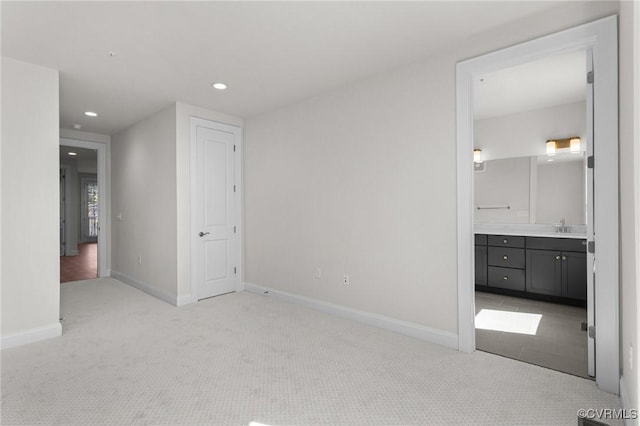 unfurnished bedroom with baseboards, light carpet, recessed lighting, ensuite bath, and a sink