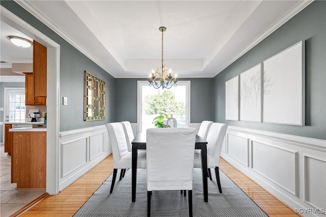 dining room with light wood-type flooring, wainscoting, a decorative wall, a raised ceiling, and a chandelier