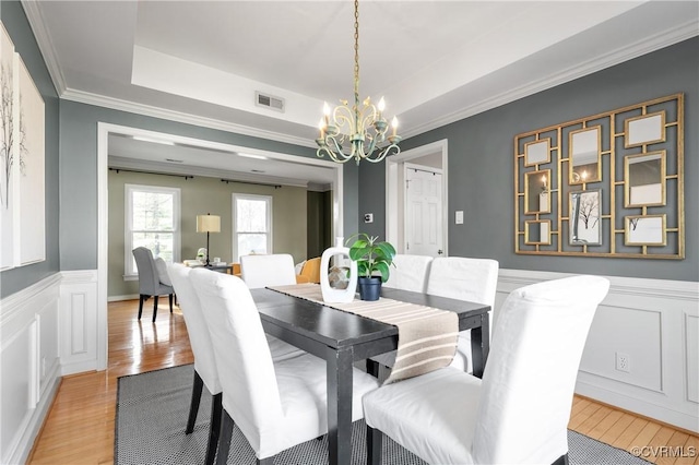 dining room with a tray ceiling, visible vents, light wood-type flooring, and a chandelier