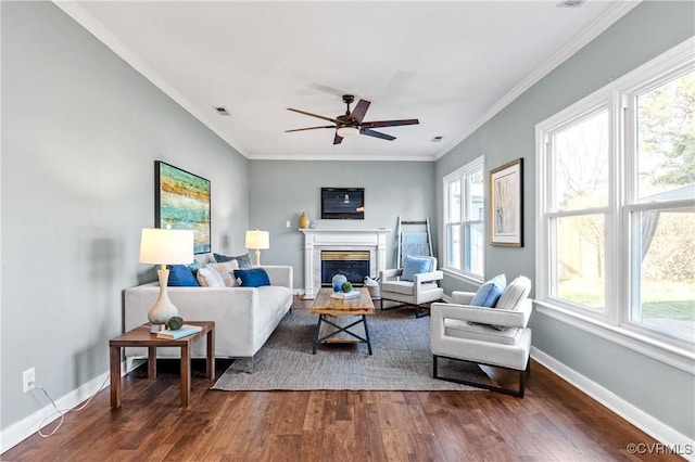 living room featuring visible vents, dark wood-type flooring, a glass covered fireplace, crown molding, and baseboards