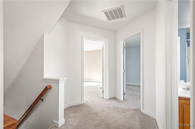 hallway featuring baseboards, an upstairs landing, visible vents, and light carpet