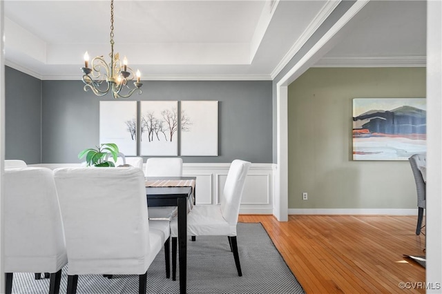 dining space featuring a chandelier, ornamental molding, a tray ceiling, and wood finished floors