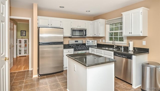 kitchen featuring a kitchen island, a sink, tile patterned flooring, appliances with stainless steel finishes, and white cabinetry