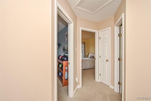 hallway with attic access, baseboards, and light carpet