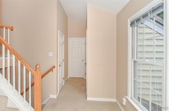 hallway featuring baseboards, light carpet, and stairs