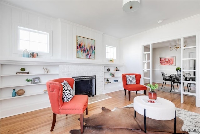 sitting room with a brick fireplace, light wood finished floors, and ornamental molding