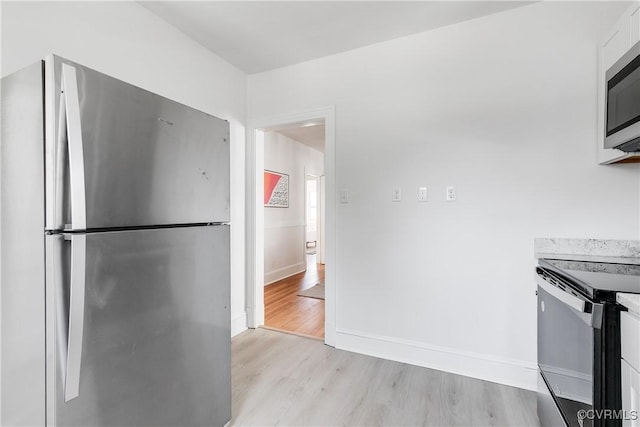 kitchen with light wood-style flooring, stainless steel appliances, white cabinets, light countertops, and baseboards