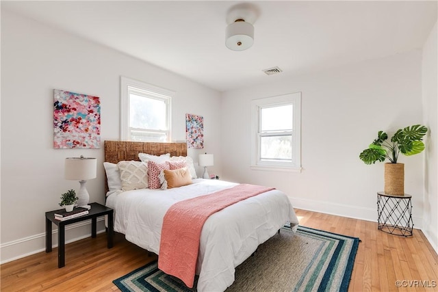 bedroom featuring visible vents, multiple windows, light wood-style floors, and baseboards