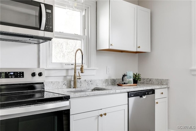 kitchen with light stone counters, appliances with stainless steel finishes, white cabinetry, and a sink