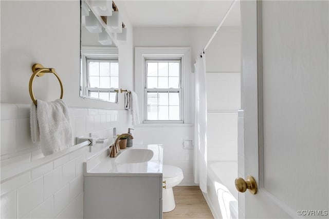 bathroom featuring vanity, wood finished floors, shower / bath combo, tile walls, and toilet