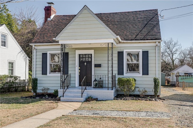 bungalow featuring a front lawn, a chimney, and a shingled roof