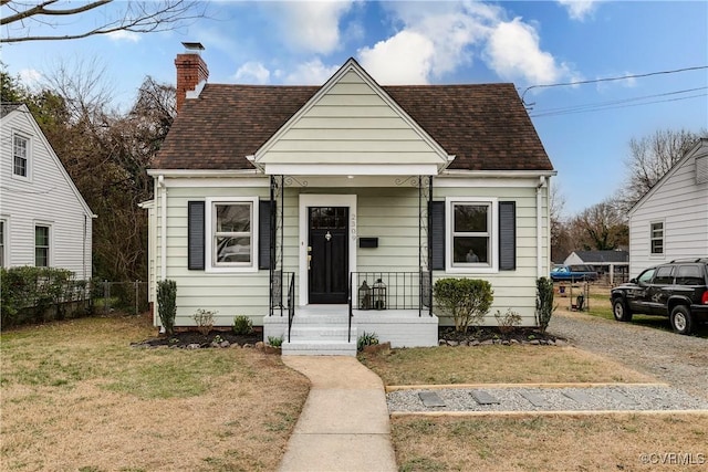 bungalow-style house with a shingled roof, a front yard, fence, and a chimney