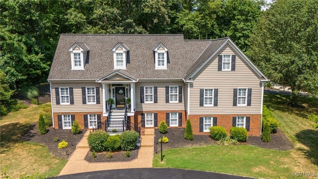 view of front of property featuring brick siding, roof with shingles, and a front lawn