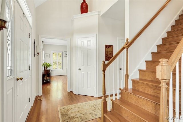 entryway featuring a towering ceiling, baseboards, light wood-style flooring, and stairs