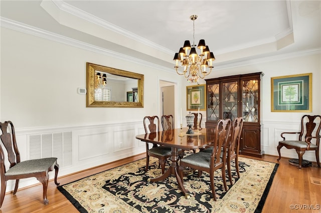 dining area with visible vents, a raised ceiling, a notable chandelier, and light wood finished floors