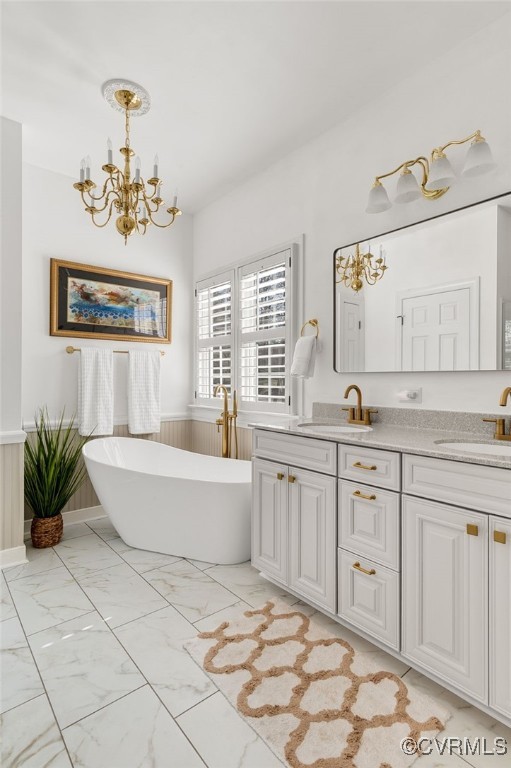 full bath featuring a freestanding bath, double vanity, marble finish floor, and a sink