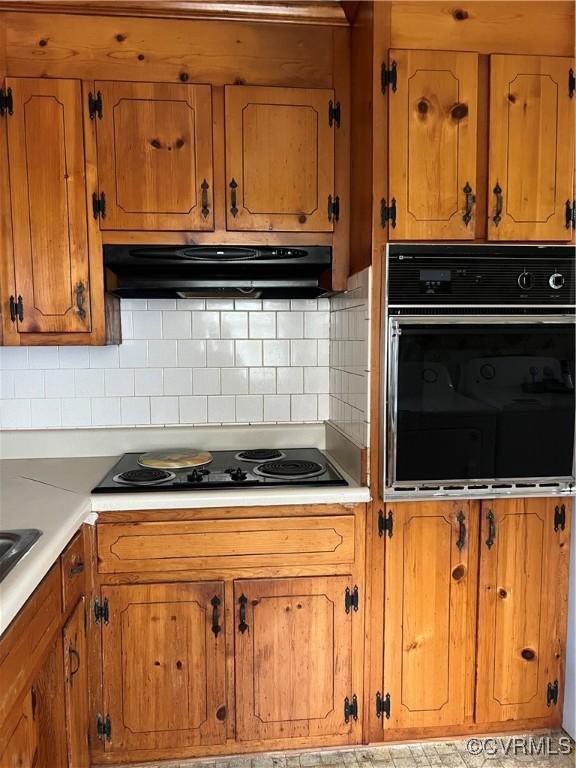 kitchen featuring under cabinet range hood, black appliances, brown cabinetry, and light countertops