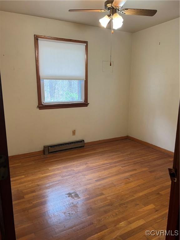 spare room with a baseboard heating unit, wood finished floors, baseboards, and ceiling fan