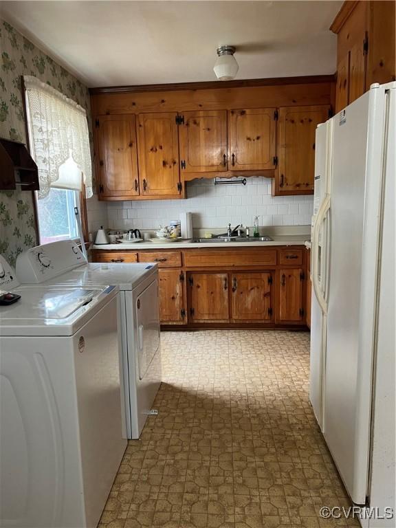 laundry area featuring light floors, wallpapered walls, cabinet space, separate washer and dryer, and a sink