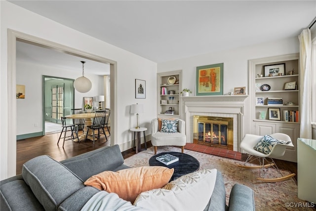 living room with a fireplace, built in features, wood finished floors, and baseboards