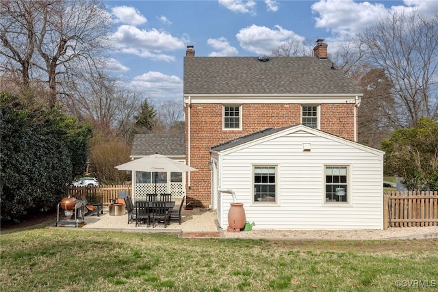 rear view of house with a patio, a lawn, brick siding, and a chimney