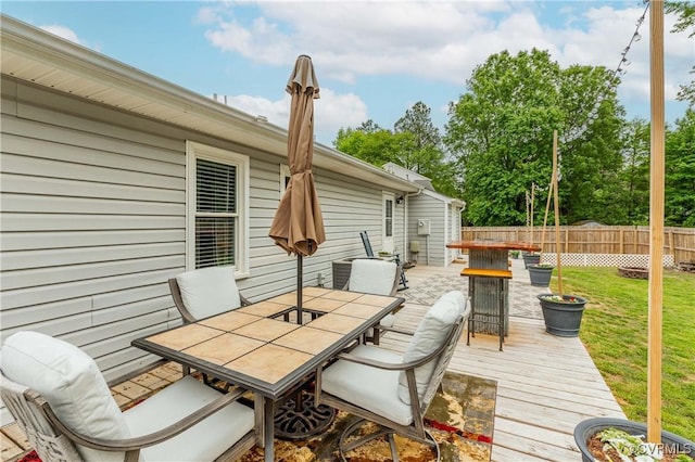 wooden terrace with outdoor dining area, a lawn, and fence