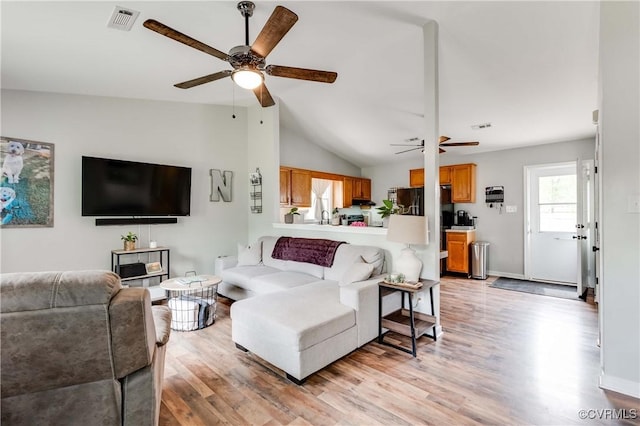 living area featuring visible vents, ceiling fan, light wood-style floors, and vaulted ceiling