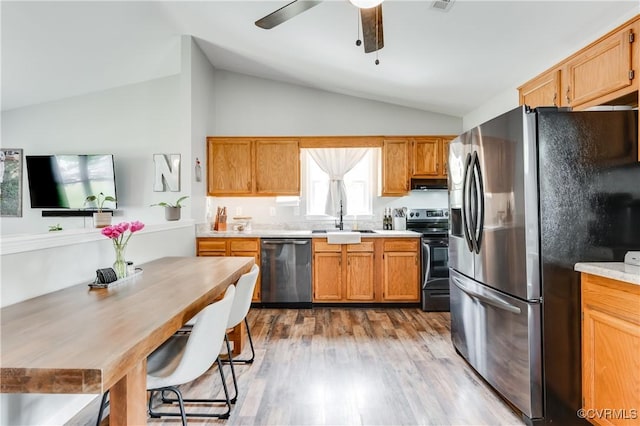 kitchen with a sink, wood finished floors, stainless steel appliances, light countertops, and vaulted ceiling