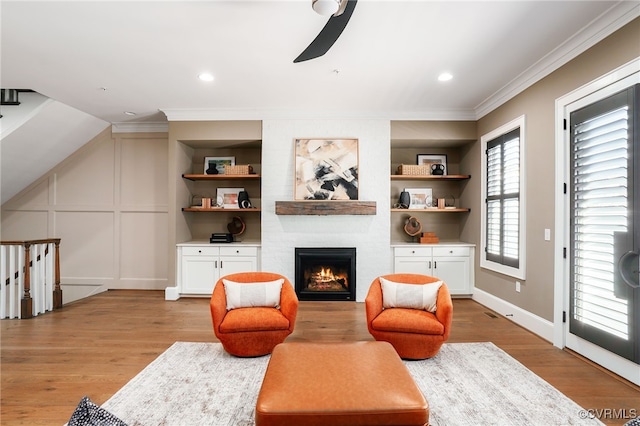 sitting room featuring light wood-type flooring, ornamental molding, built in features, a fireplace, and a decorative wall