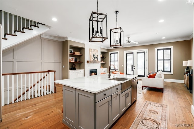 kitchen featuring light wood-type flooring, gray cabinets, a sink, crown molding, and open floor plan