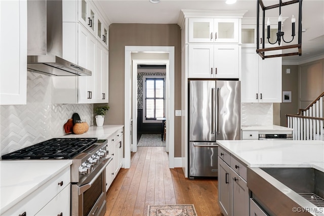 kitchen featuring light wood-type flooring, white cabinets, stainless steel appliances, and wall chimney exhaust hood