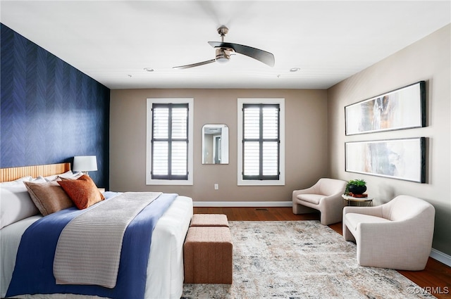 bedroom with wallpapered walls, an accent wall, baseboards, and wood finished floors