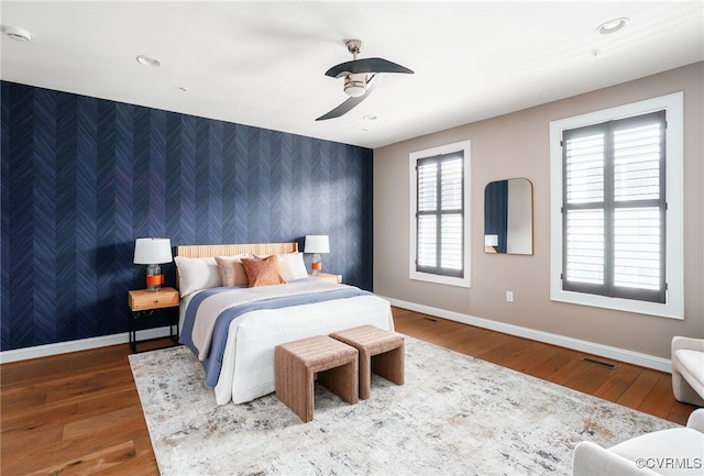 bedroom with visible vents, wallpapered walls, an accent wall, baseboards, and hardwood / wood-style floors