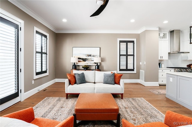 living area with visible vents, light wood-type flooring, baseboards, and ornamental molding