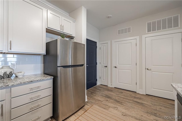 kitchen featuring light wood finished floors, visible vents, tasteful backsplash, and freestanding refrigerator