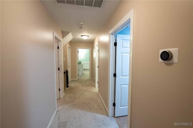 hallway with baseboards, visible vents, and light carpet