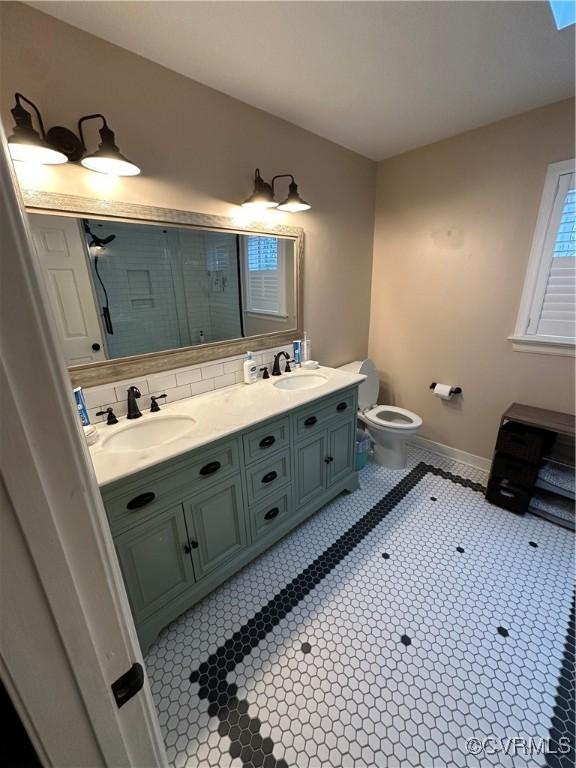 bathroom featuring a sink, tasteful backsplash, toilet, and double vanity