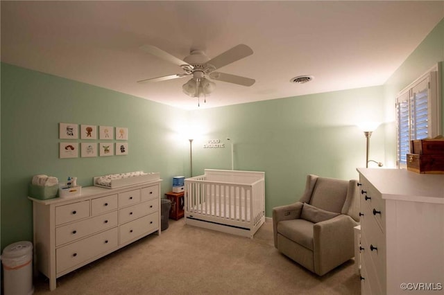 bedroom with visible vents, a crib, light colored carpet, and a ceiling fan