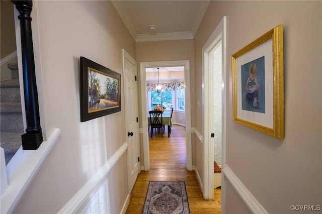 hallway featuring baseboards, a chandelier, stairway, light wood-type flooring, and ornamental molding