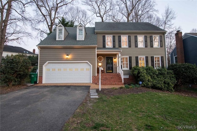 colonial house featuring aphalt driveway, an attached garage, a shingled roof, and a front yard