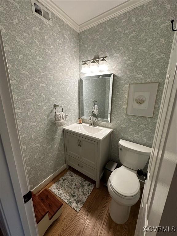 half bathroom featuring visible vents, wood finished floors, crown molding, and wallpapered walls